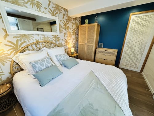Chambre La Bounty de La Villa Plein Vent avec lit en rotin, papier peint tropical, mur d'accent vert canard et vue sur le jardin