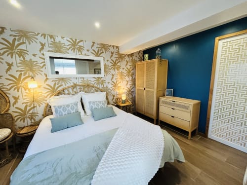 Chambre de la villa La Bounty à La Villa Plein Vent avec papier peint tropical, mur d'accent bleu, mobilier en bois et vue sur le jardin