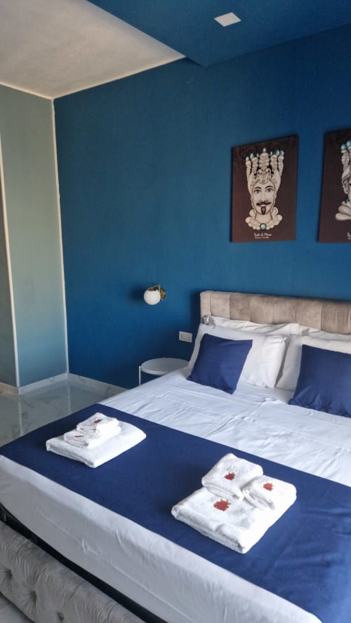 Camera da letto moderna blu presso U Baruni B&B a Messina con letto queen, biancheria bianca, cuscini decorativi e quadri