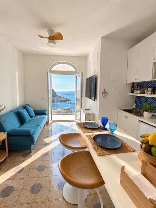 Appartamento vista mare a Ischia con divano blu, cucina e splendida vista sul mare attraverso le porte ad arco di Chiaia di Rose