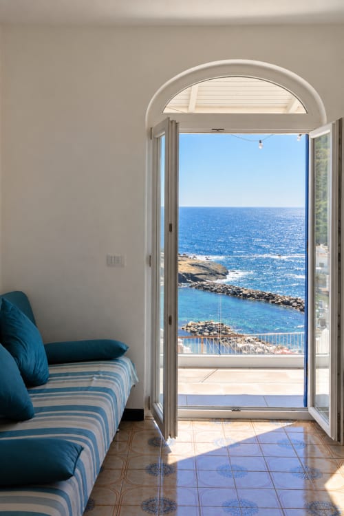 Camera da letto sul mare dell'appartamento di Ischia con letto a righe blu, arco che si apre sul balcone con vista sul Mar Mediterraneo