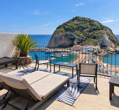 Terrazza sul mare a Chiaia di Rose, Ischia con lettini, zona ristorazione e vista sulla baia turchese e collina verdeggiante