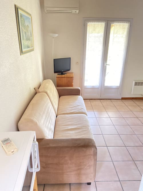 Salón con sofá beige, televisor y puertas de cristal en el apartamento Domaine de la Bégude, Fayence