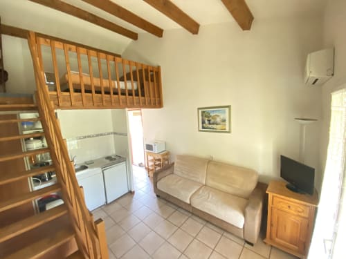 Apartamento del Domaine de la Bégude con sofá beige, cocineta, vigas de madera y televisión en Fayence