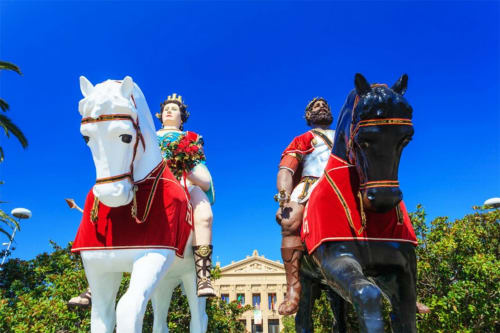 Due figure romane a cavallo, uno bianco e uno nero, in mantelli rossi vicino a un edificio classico a Messina
