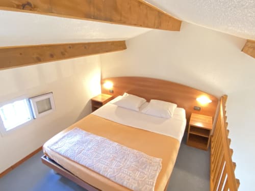 Chambre avec poutres en bois, lit double, draps blancs, lampes de chevet et plafond mansardé au gîte Domaine de la Bégude