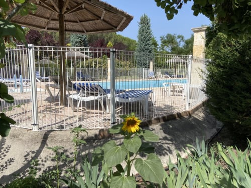 Área de piscina vallada en Domaine de la Bégude con tumbonas, sombrilla y girasol en primer plano, FAYENCE