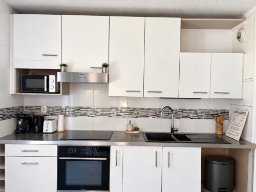 Cuisine blanche moderne avec appareils en acier inoxydable et comptoirs gris à l'appartement Le Paradis Des Logis, Pierrefitte sur