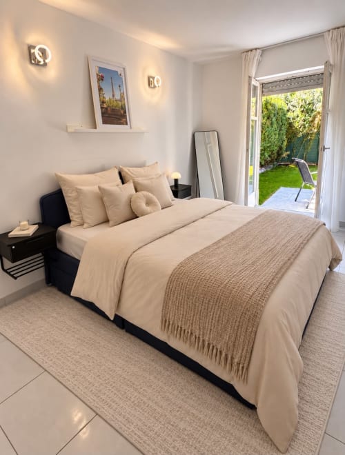 Chambre moderne à Le Paradis Des Logis avec vue sur le jardin, literie crème, table de nuit noire et portes-fenêtres donnant sur la terrasse