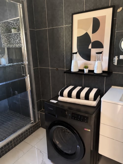 Salle de bains moderne au Paradis Des Logis avec lave-linge noir, serviettes rayées, art géométrique mural et carrelage sombre