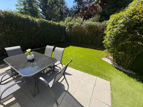 Terrasse ensoleillée du Paradis Des Logis avec table à diner, chaises et pelouse soignée bordée de haies