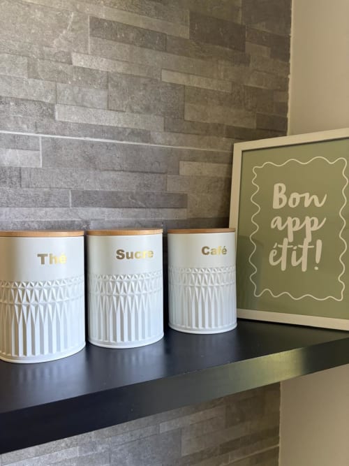 Trois bocaux de cuisine blancs étiquetés Thé, Sucre et Café avec accents dorés dans l'appartement Le Paradis Des Logis à Pierrefitte