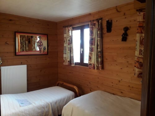 Chambre cosy au mobilier rustique de La Ferme Buissonnière avec lits jumeaux, vue sur les montagnes et murs en bois de pin