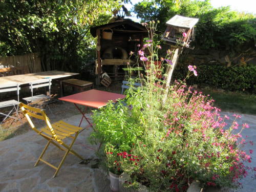 Terrasse rustique du gîte La Ferme Buissonnière à Biol avec fleurs roses, chaise jaune et structures fermières.