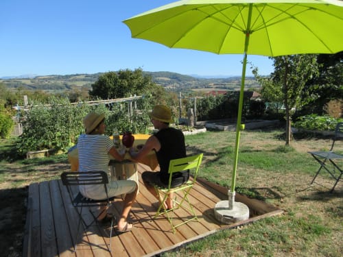 Deux hôtes se détendent sous un parasol vert citron sur une terrasse en bois à La Ferme Buissonnière, avec les collines toscanes