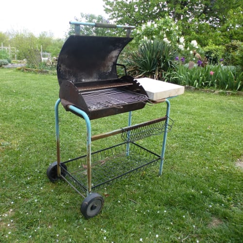 Barbecue tonneau noir avec table latérale et étagères de rangement sur l'herbe à La Ferme Buissonnière, Biol France