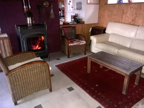 Salon douillet à la Ferme Buissonnière avec cheminée, fauteuils en osier, canapé crème et tapis bourgogne, Biol