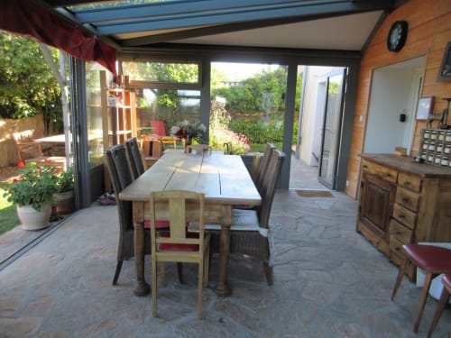 Véranda lumineuse et ensoleillée du gîte La Ferme Buissonnière à Biol avec mobilier en bois et vue sur le jardin