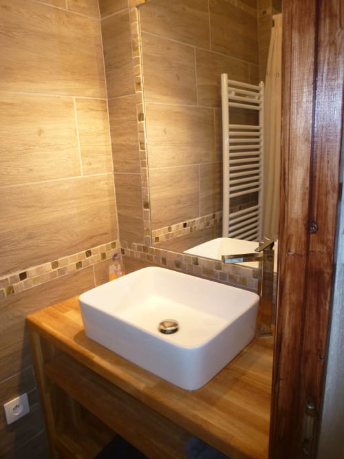 Salle de bains rustique au gîte La Ferme Buissonnière à Biol avec murs en carrelage bois, lavabo blanc et porte-serviettes chauffant