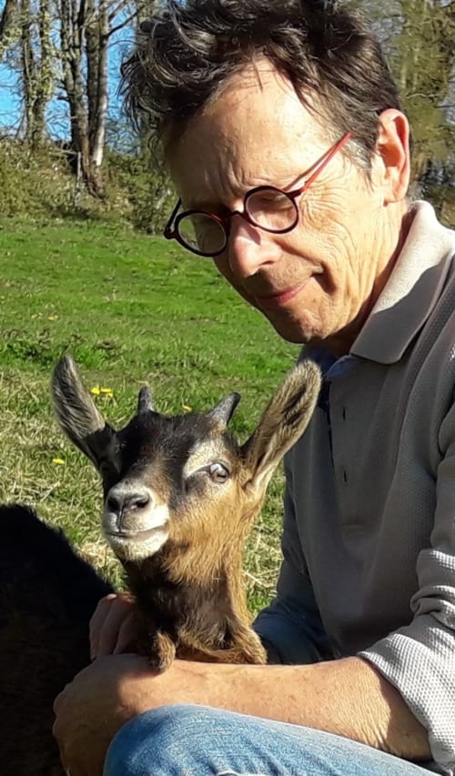 Homme avec des lunettes tenant une chèvre à La Ferme Buissonnière, gîte rural à Biol, France