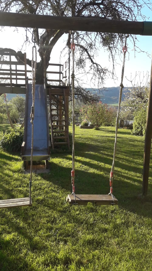 Balançoire rustique en bois suspendue à une branche d'arbre dans les prairies de La Ferme Buissonnière avec vue sur les montagnes, Biol