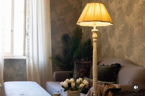 Camera elegante alle Seven Suites Sanremo con lampada da terra dorata, pianta in vaso, fiori bianchi e vista sulla città