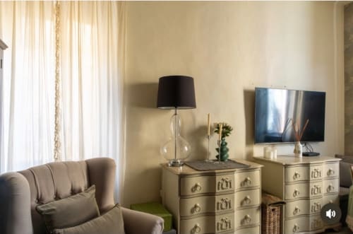 Elegante soggiorno dell'appartamento SEVEN SUITES SANREMO con divano beige, cassettone in legno, lampada, TV schermo piatto e vista sulla città