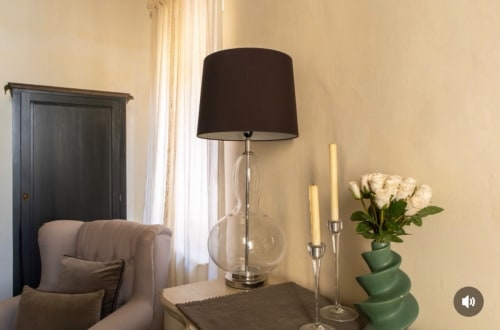 Interno elegante del SEVEN SUITES SANREMO con poltrona rivestita, lampada da tavolo, rose bianche e candelabri