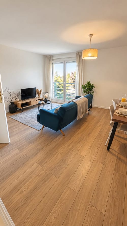 Salon moderne avec fauteuil bleu, parquet, table à manger, télévision, suspension et balcon avec vue sur le jardin