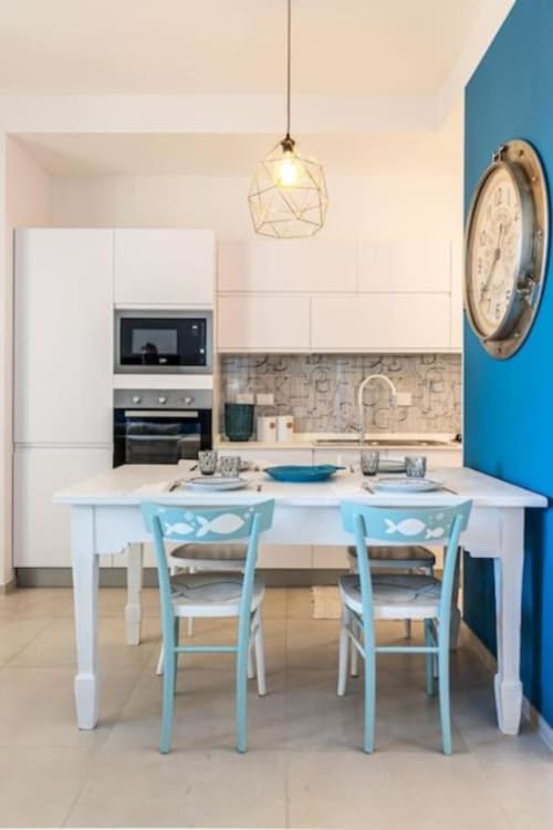 Zona cucina-sala da pranzo moderna alle SEVEN SUITES SANREMO con tavolo bianco, sedie turchesi, lampada a sospensione geometrica e blu