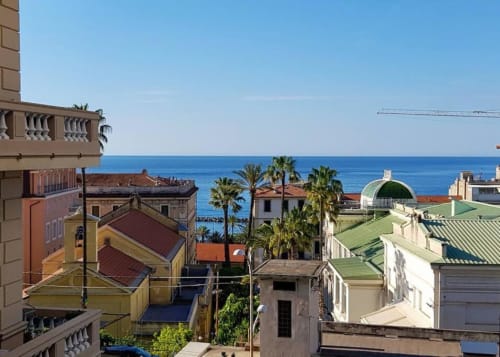 Vista sul mare dal balcone dei Seven Suites Sanremo con palme e edifici colorati a Sanremo, Italia