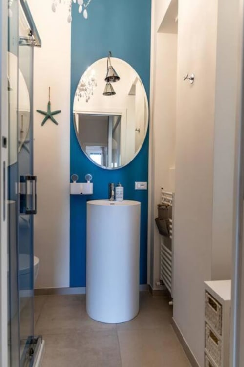 Bagno moderno del SEVEN SUITES SANREMO con parete in blu, lavabo cilindrico bianco, specchio rotondo e arredamento costiero
