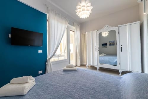 Camera moderna alle SEVEN SUITES SANREMO con parete d'accento teal, letto blu-grigio, guardaroba bianco e balcone con vista mare.