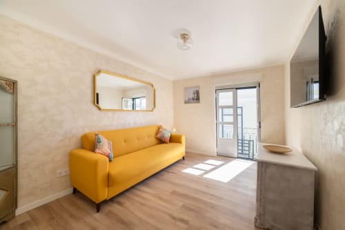 Bright living room in Lisboa hostel apartment with yellow sofa, golden mirror, wooden floors, and balcony access