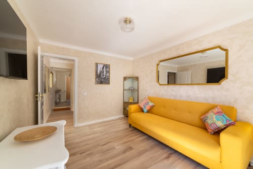 Bright yellow sofa in modern Lisbon hostel apartment with wooden floors, mirror, and open living area
