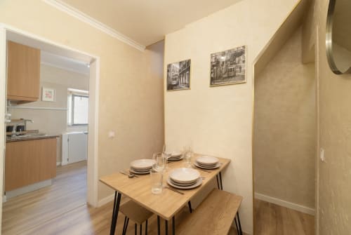 Dining area in Bica Mini Hostel apartment, Lisboa with wooden table, place settings, and kitchen visible through doorway