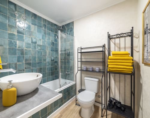 Modern bathroom at Bica Mini Hostel Lisboa with teal tile shower, round vessel sink, yellow towels, and metal storage