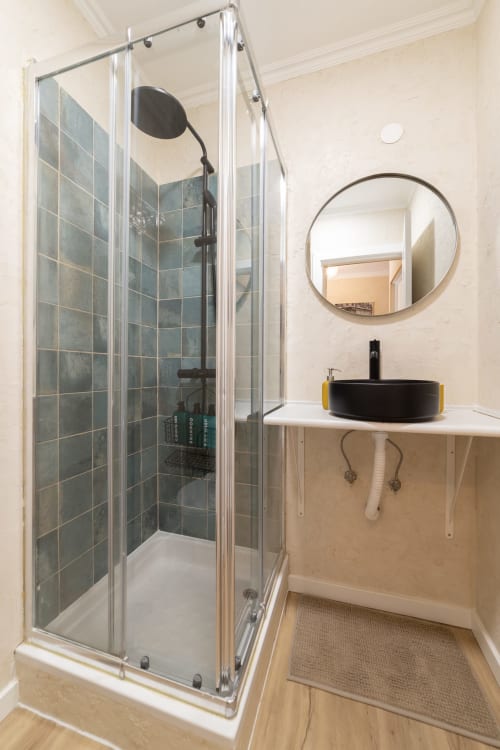Modern bathroom in Bica Mini Hostel, Lisboa with glass shower enclosure, black sink, and round mirror