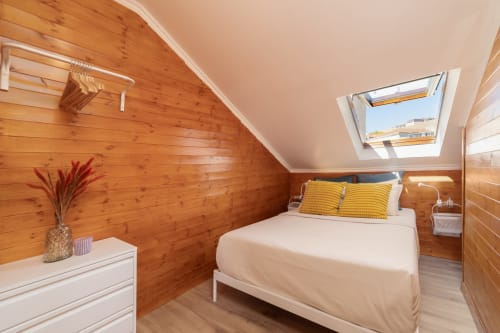 Bright attic bedroom at Bica Mini Hostel Lisboa with wood walls, skylight, queen bed, yellow pillows, and white dresser