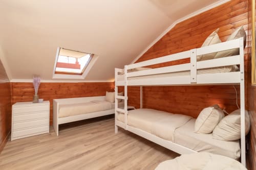 Bright attic bedroom at Bica Mini Hostel Lisboa with white bunk beds, wooden beams, skylights, and modern furnishings