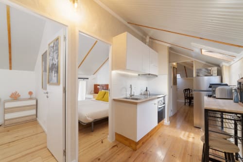 Modern 2-bedroom apartment in Lisbon with open-plan kitchen, bedroom with yellow pillows, hardwood floors, and bright natural