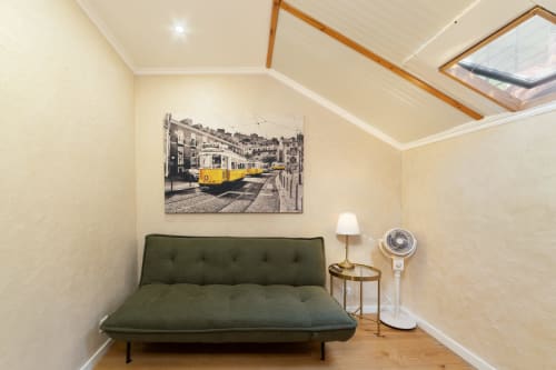 Modern hostel bedroom in Lisbon with green sofa, yellow tram artwork, wooden floors, and skylight window