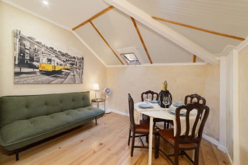Lisbon apartment with green sofa, wooden dining table, yellow tram artwork, vaulted ceiling with skylights, and hardwood