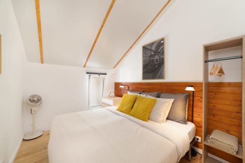 Modern bedroom in Lisbon Central Apartments hostel with wooden headboard, yellow pillows, white bedding, and sloped wooden