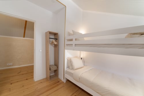 Modern hostel bedroom in Lisbon with white bunk bed, wooden floor, and compact wardrobe storage.