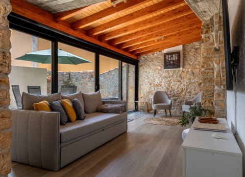 Lounge moderno em Recantos D'Almerinda com paredes de pedra à vista, teto de vigas de madeira, assentos cinza e grandes janelas