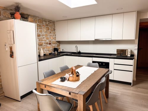 Cozinha moderna branca com bancada preta, mesa de jantar em madeira e parede de tijolos aparentes no hotel Recantos D'Almerinda