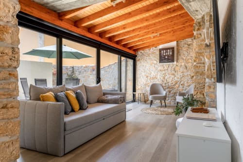 Sala de estar moderna no Recantos D'Almerinda em Pombal com paredes de pedra, vigas de madeira, sofá cinzento e acesso ao terraço.