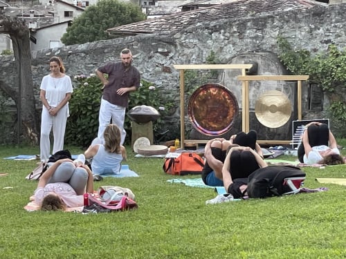 Group yoga session on lawn at Roseto del Drago B&B in Ponte In Valtellina with gongs and stone buildings
