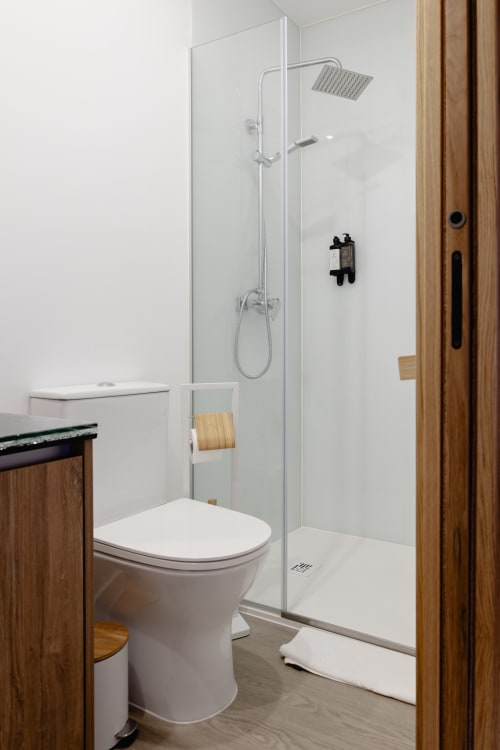 Banheiro moderno em Recantos D'Almerinda com box de vidro, vaso sanitário branco, gabinete de madeira e chuveiro cascata.